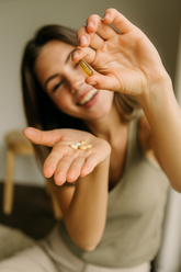 Woman holding a supplement pill between her fingers with a neutral background